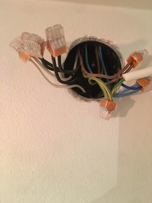 Öppen kopplingsdosa med flera elanslutningar och orange skarvklämmor på en vit vägg, som relaterar till en fråga om elinstallation.