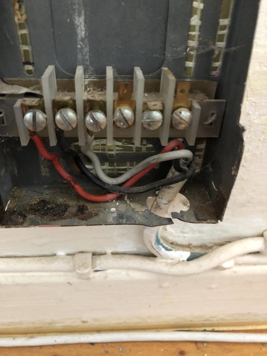 Gammal elinstallation med synliga trådar och skruvanslutningar, med röda och svarta kablar mot en sliten trävägg.