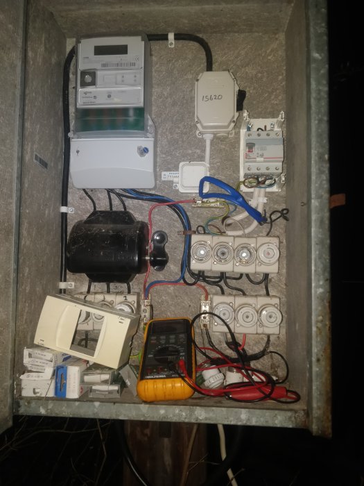 Elcentral med öppet säkringsskåp, olika säkringar och en multimeter.