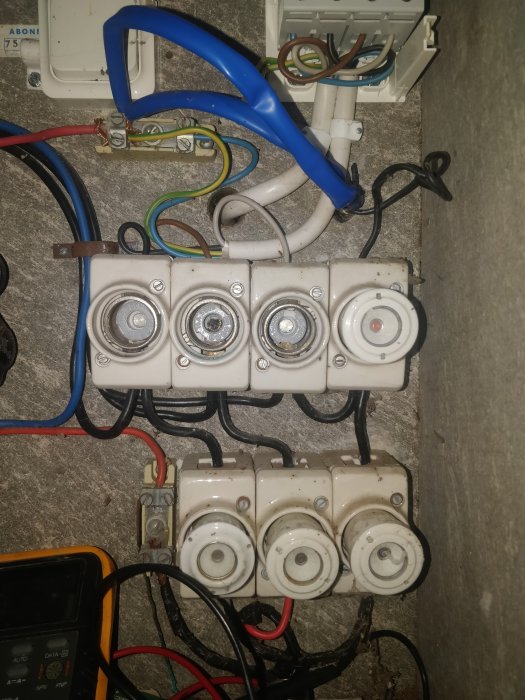 Gamla keramiska säkringar i säkringsskåp med synliga ledningar och mätinstrument.