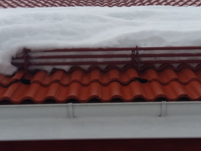 Tak med snötäcke och trasiga takpannor nära snörasskydd på ett nybyggt hus.