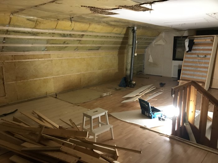 Övervåning under renovering med isolerade väggar och utspridda byggmaterial.