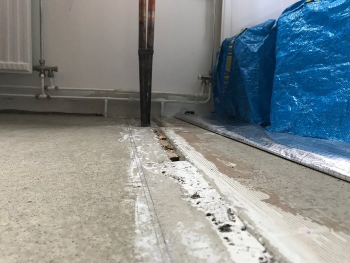Ojämnt betonggolv med synlig skarv och spår efter borttagen glasvägg, nära ett upptäckt rör och blå presenning.