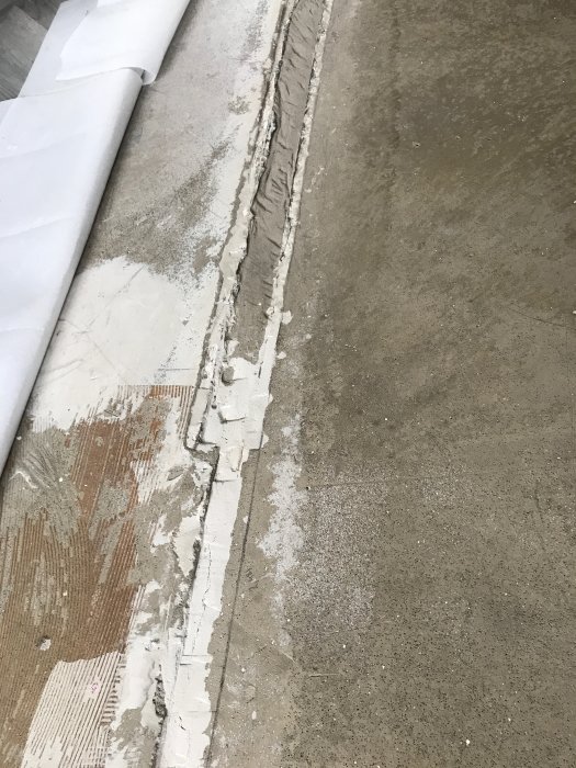 Betonggolv med en tydlig skarv fylld med utjämningsmassa, omgiven av ojämn och delvis borttaget golv.