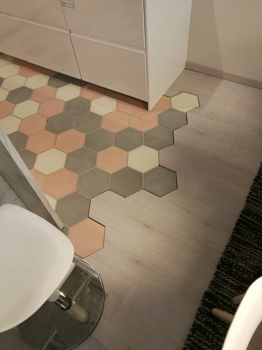Hexagonala kakelplattor i olika nyanser intill träimitation laminatgolv.