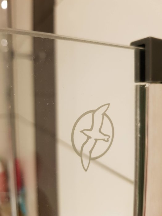 Märke på glasdörr föreställande en ring med en silhuett av en fågel inuti.