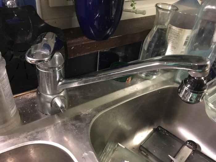 Köksblandare över diskho med olika flaskor och föremål runtomkring.