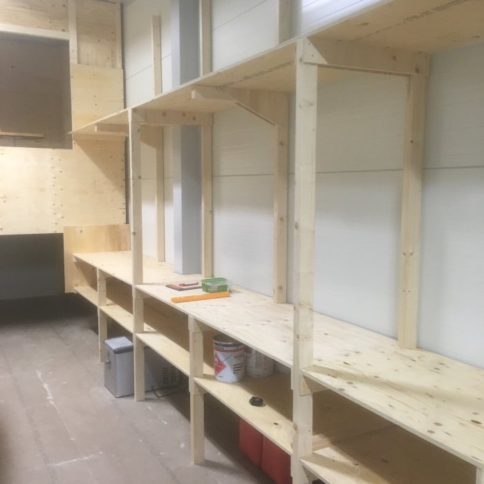 Nybyggd trähylla i ett förråd med en arbetsyta och utrymme under för förvaring av flyttlådor.