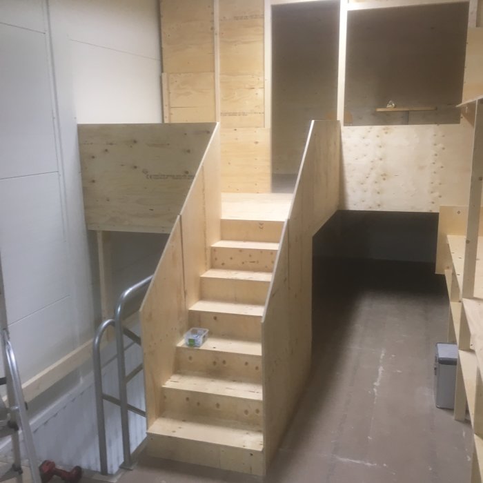 Nybyggd trähylla för lager med arbetsyta och plats för förvaring bredvid en trätrappa och räcke.