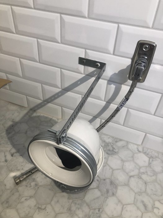 Nyinstallerad toalettstol på plastdistanser mot ett kaklat vägg och ett marmormönstrat golv under renovering.