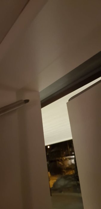 Ytterdörr som tar i karmen på övre sidan, indikerad av en pekande skruvmejsel, med kvällsvy genom fönstret.