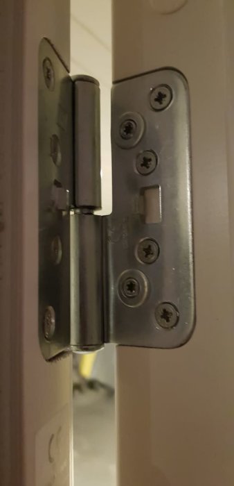 Närplan på en ytterdörrs gångjärn med synliga skruvar mot en karm.