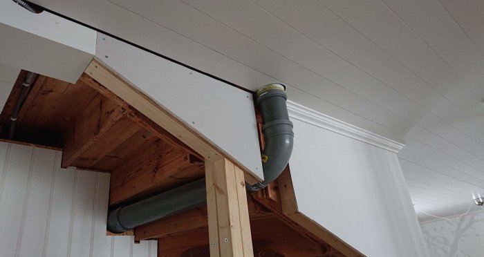 Vit panelvägg och tak med synliga spacklade skruvhål och en genomgående grå avloppsrörinstallation.