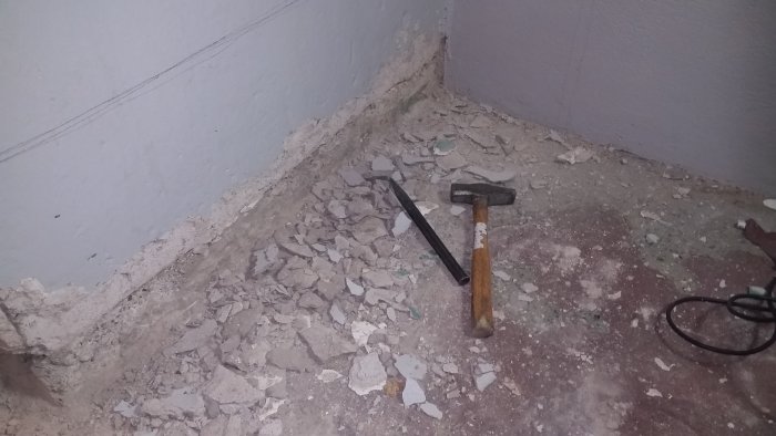 Hörn i ett rum med bortknackad puts och en slägga bredvid en hög med avlagringar.