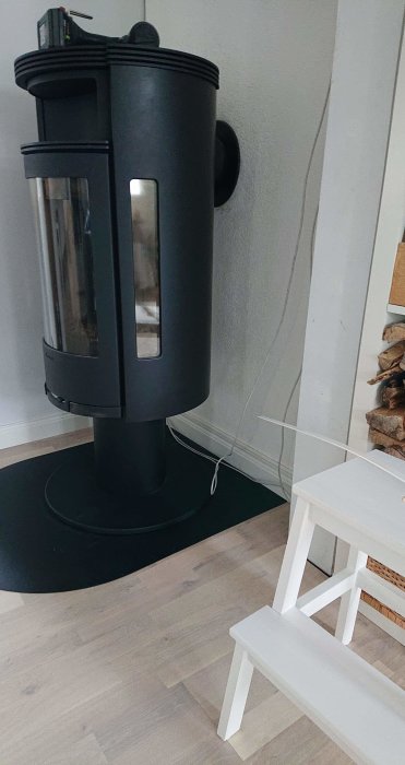 Modern svart kamin med nätverkssladdar organiserade längs väggen och vedlagring.