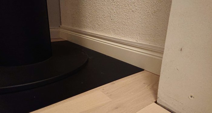 Hörn av ett rum med spacklade skruvhål, nätverkskabel bakom kamin och snyggt monterad golvlist.