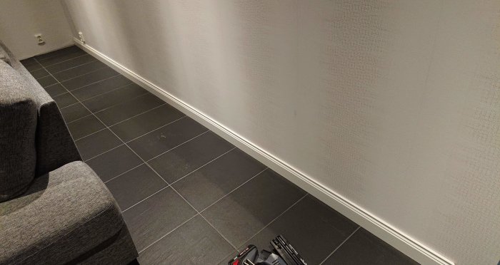 Renoverat rum med nyspacklade skruvhål och fixade hörn vid en grå texturtapet och mörkt kakelgolv.