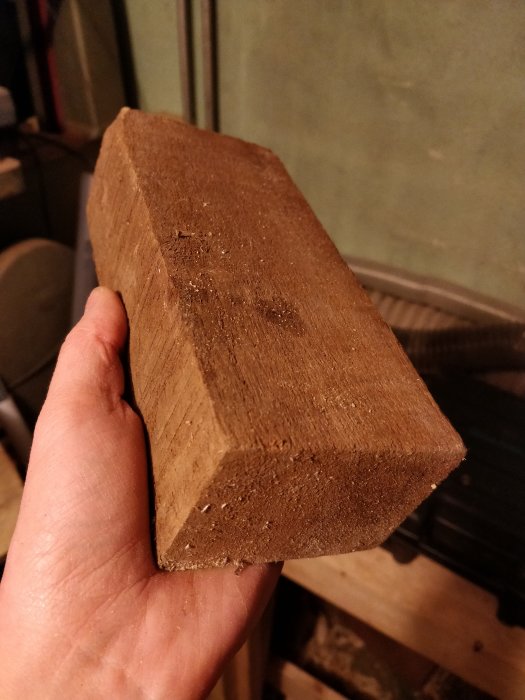 En hand håller en rektangulär teakträbit i ett rum.