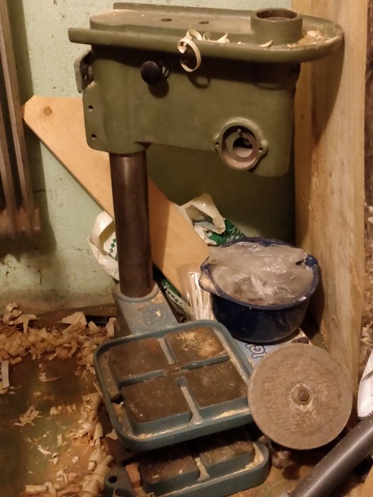 Verktyg och sågspån i hörn av verkstad, indikerar snickeriarbete och materialåtervinning.