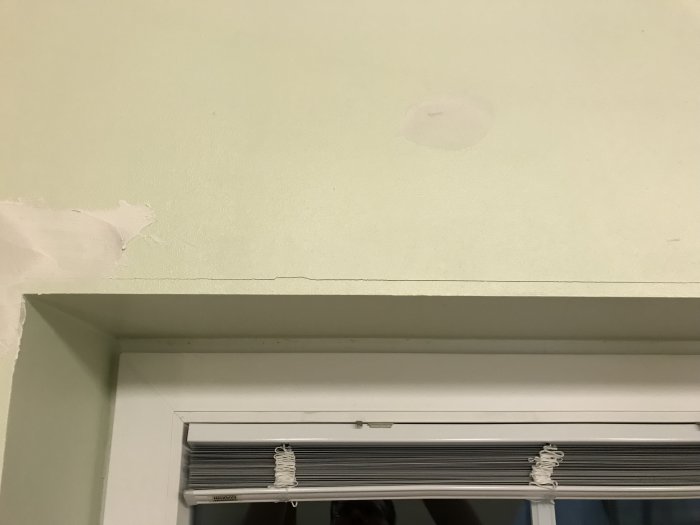 Horisontell spricka ovanför ett fönster med nymålat innertak och vägg.