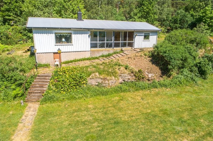 Ett litet hus med uterum sett från ovan, omgivet av en gräsmatta och träd, med en krypgrund och oisolerad betongplatta.