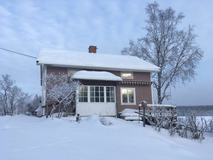 Eternithus täckt av snö med synlig tegelfasad och snölandskap runtomkring.