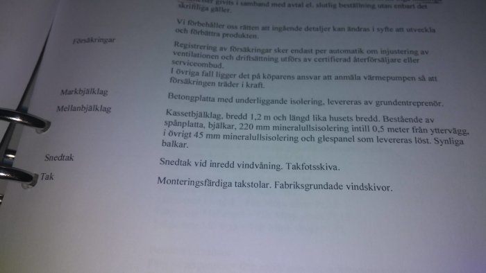 Sida med byggbeskrivning öppen i pärm med text om mellanbjälklag och isolering.