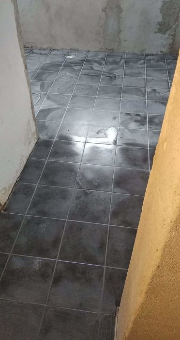 Nyfogade grå klinkergolv med synliga fogar och fuktfläckar under renoveringsarbeten.