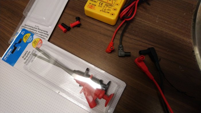 Gripklor i förpackning och multimeter med anslutna banankablar på ett bord.
