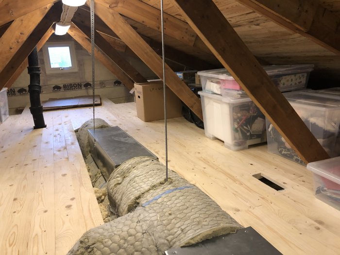 Oinredd vind med nytt råspontsgolv, lösullsisolering på sidan och förvaringslådor under snedtaket.