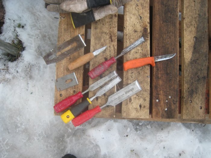 Verktyg som moraknivar och stämjärn utspridda på en träpall i snön som en del av verktygsvård.