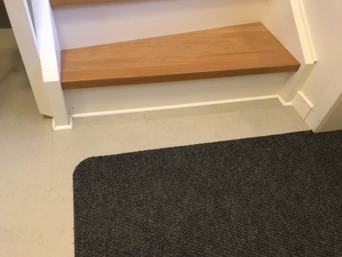 Trappsteg med ljust trä, vit kvartsstav provlagd för fix efter golvläggning mot grå heltäckningsmatta.