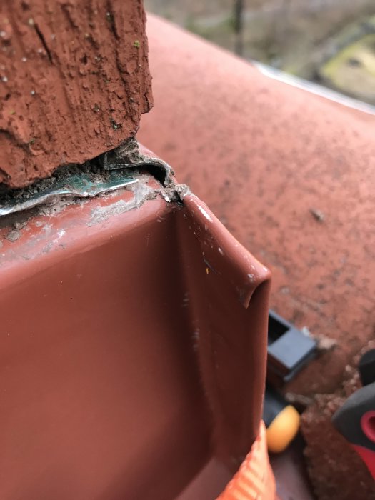 Närbild på saknad tätning där takplåt möter tegelsten.