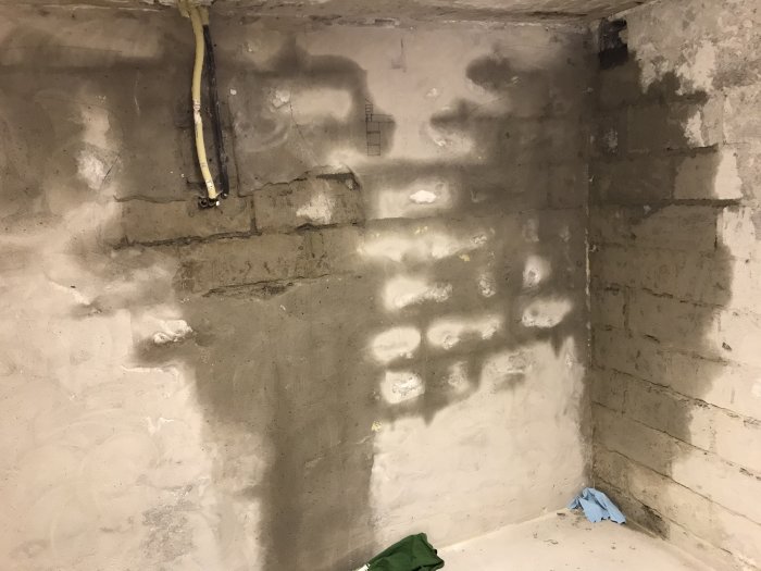 Fuktmerker på betongvegg i et kjellerrom. Våt flekk sprer seg fra hjørnet, indikerer muligens lekkasje. Rør på toppen av veggen.