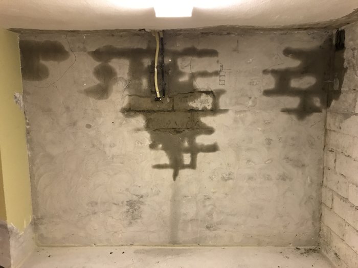 Fuktig betongvegg i kjeller med spor av vanninntrenging, usannsynlig pga manglende fuktsperre. Teglvegg over mistenkes som kilde til problemet.