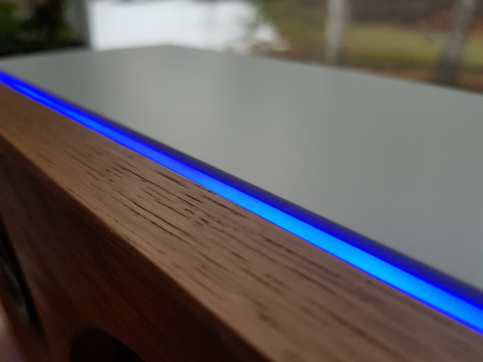 Högkvalitativ detalj av hemgjord blåtandshögtalare med belyst blå LED-strip bakom genomfrostad akryl och ekfront.