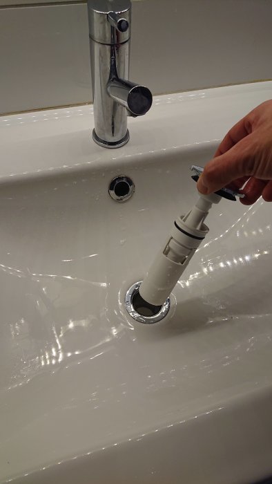 Hand som lyfter ett Prevex vattenlås ur ett handfat under installation eller underhåll.