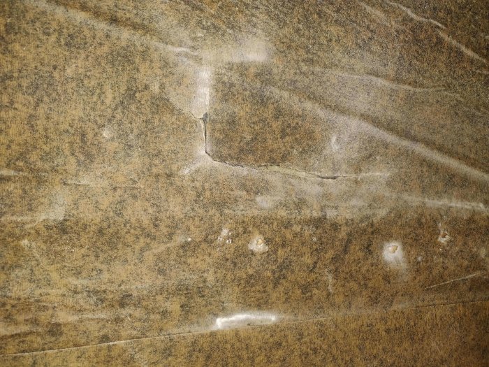 Närbild på en bruna byggpapp med skador, som används för isolering bakom en gipsvägg.