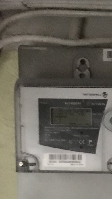 Otydlig bild på en elektrisk elmätare med kablar och etiketter på en vägg.