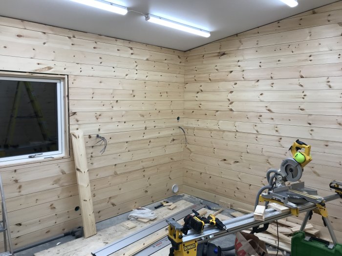 En nästan färdigställd väggpanel i ett arbetsrum med verktyg och ofärdig ventilation.