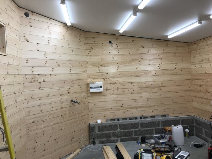 Nybyggd vägg med träpanel och pågående installation av ventilation i ett verkstadsrum.
