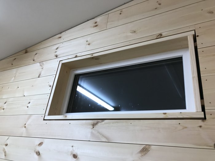 Väggpanel av trä med infälld fönsternisch och invändig smyg, ej fullständigt installerad ventilation.