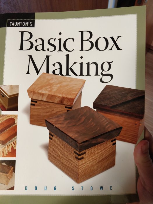 Hand håller en bok med titeln "Basic Box Making" med bilder på olika träaskar på omslaget.