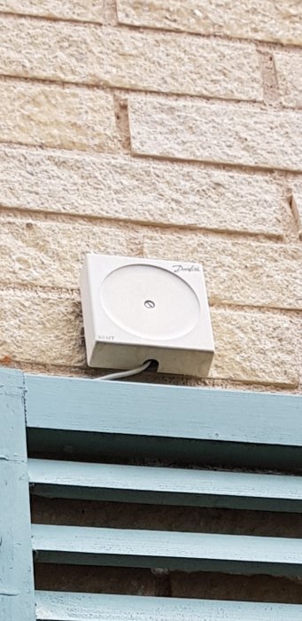 En vit dosa eller sensor monterad på en ljus tegelvägg ovanför en blå träplank.