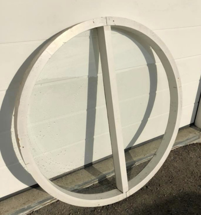 Runt träfönster med en glasruta, 138 cm i diameter, behöver målas, står mot en vit vägg.