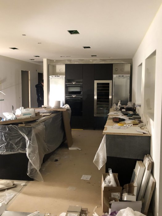 Kök under renovering med synliga inbyggda vitvaror och byggmaterial utspridda på golv och ytor.