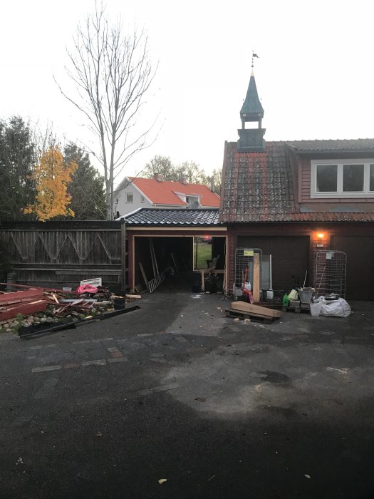 Uppfart med utsikt mot en byggnad under renovering, saknade grindar och dörr, byggmaterial utspritt framför carporten.