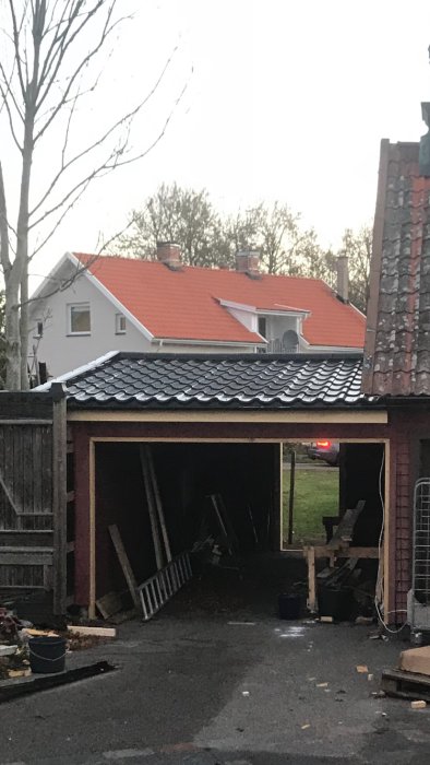 Oavslutat carporttak med öppen baksida och tillfälliga trästöd, omringat av blandad bråte.