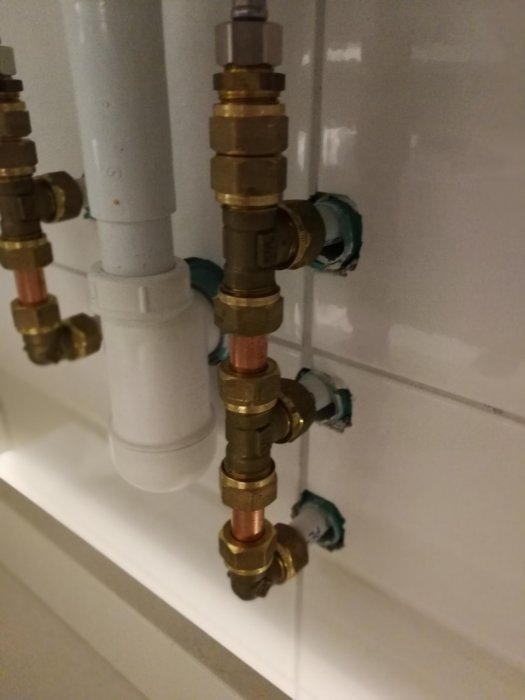 Vattenrör utan silikonfog där de går in i en vit vägg i ett badrum.