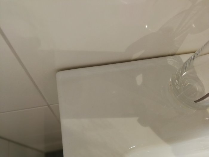 Vit kaklad badrumsvägg utan silikonfog där handfat möter väggen, synlig springa.